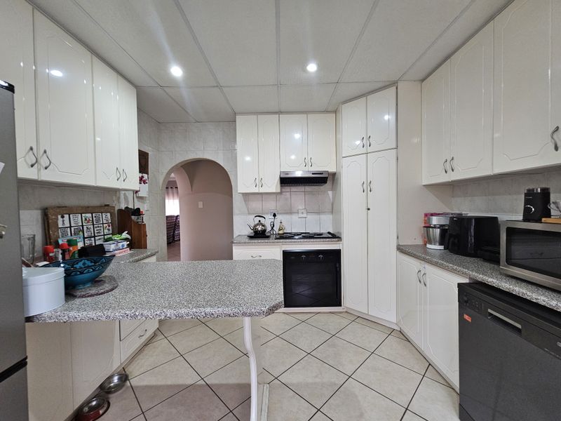 A functional kitchen featuring white cabinetry, granite countertops, built-in oven, hob, and tiled flooring, with an open archway leading to adjacent living areas.