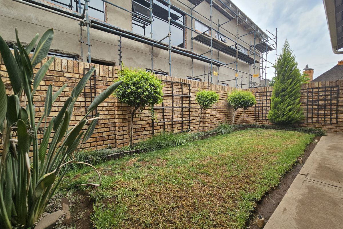 Rear garden area featuring a face brick boundary wall with trellis and lawn, currently undergoing exterior building maintenance with scaffolding in place.