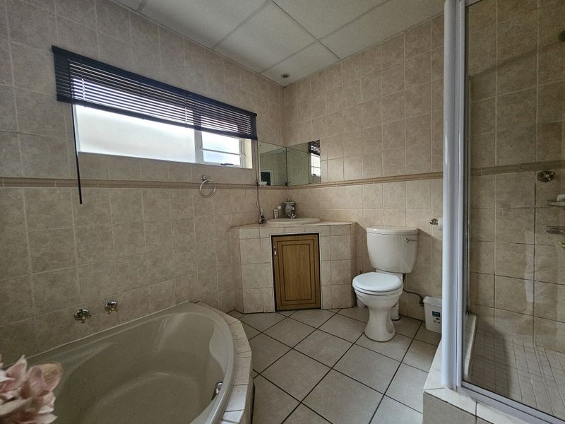 A functional bathroom featuring a corner bathtub, separate shower enclosure, toilet, and a built-in vanity unit with tiled finishes.