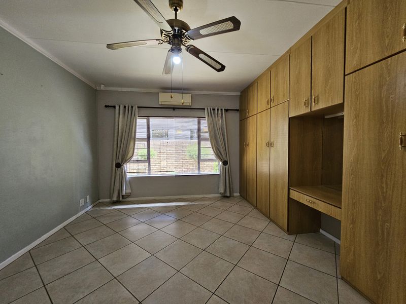 Spacious bedroom featuring extensive built-in wooden cabinetry, a built-in desk, tiled flooring, ceiling fan, and a wall-mounted air conditioning unit.