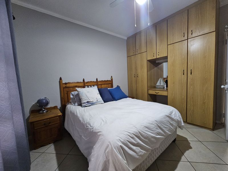 A bedroom featuring built-in wooden cupboards, a ceiling fan, and tiled flooring.