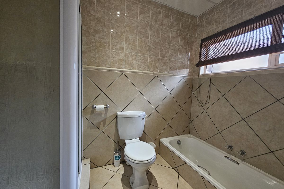 A functional bathroom featuring a built-in bathtub, separate shower enclosure, and neutral ceramic tiling throughout.