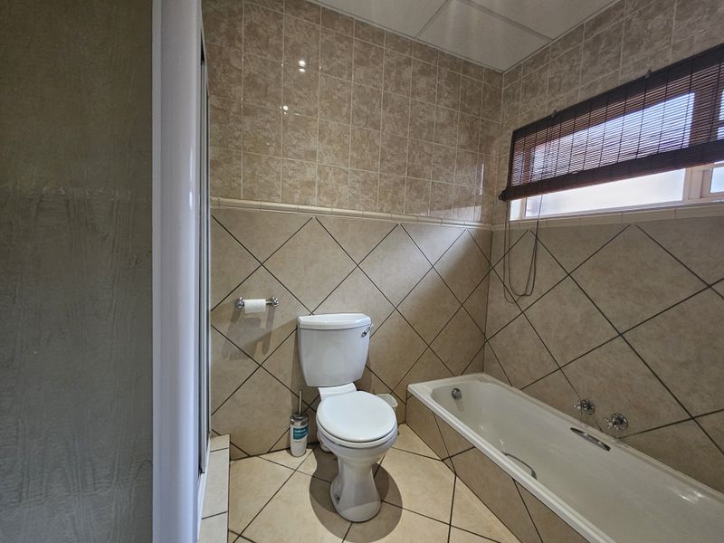 A functional bathroom featuring a built-in bathtub, separate shower enclosure, and neutral ceramic tiling throughout.
