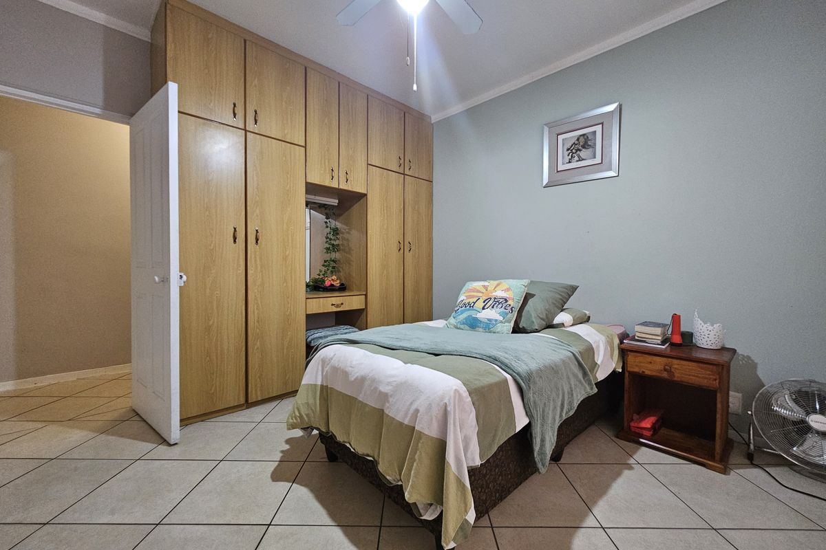 A bedroom featuring built-in wooden cupboards with a vanity section, tiled flooring, and a ceiling fan.
