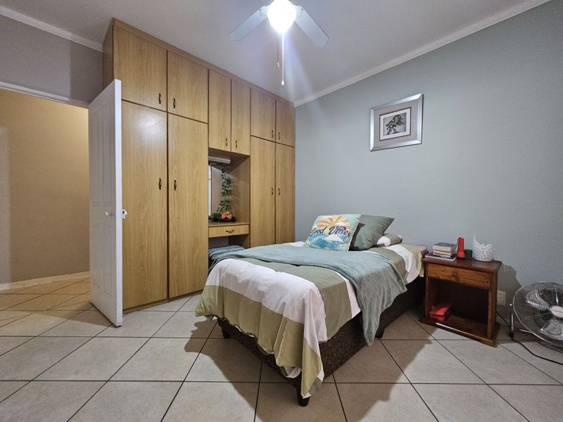 A bedroom featuring built-in wooden cupboards with a vanity section, tiled flooring, and a ceiling fan.