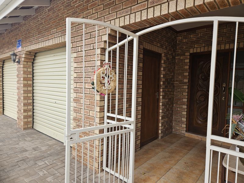 Front entrance area featuring a face brick facade, paved driveway, roll-up garage door, and a secure gated porch with a decorative wooden front door.