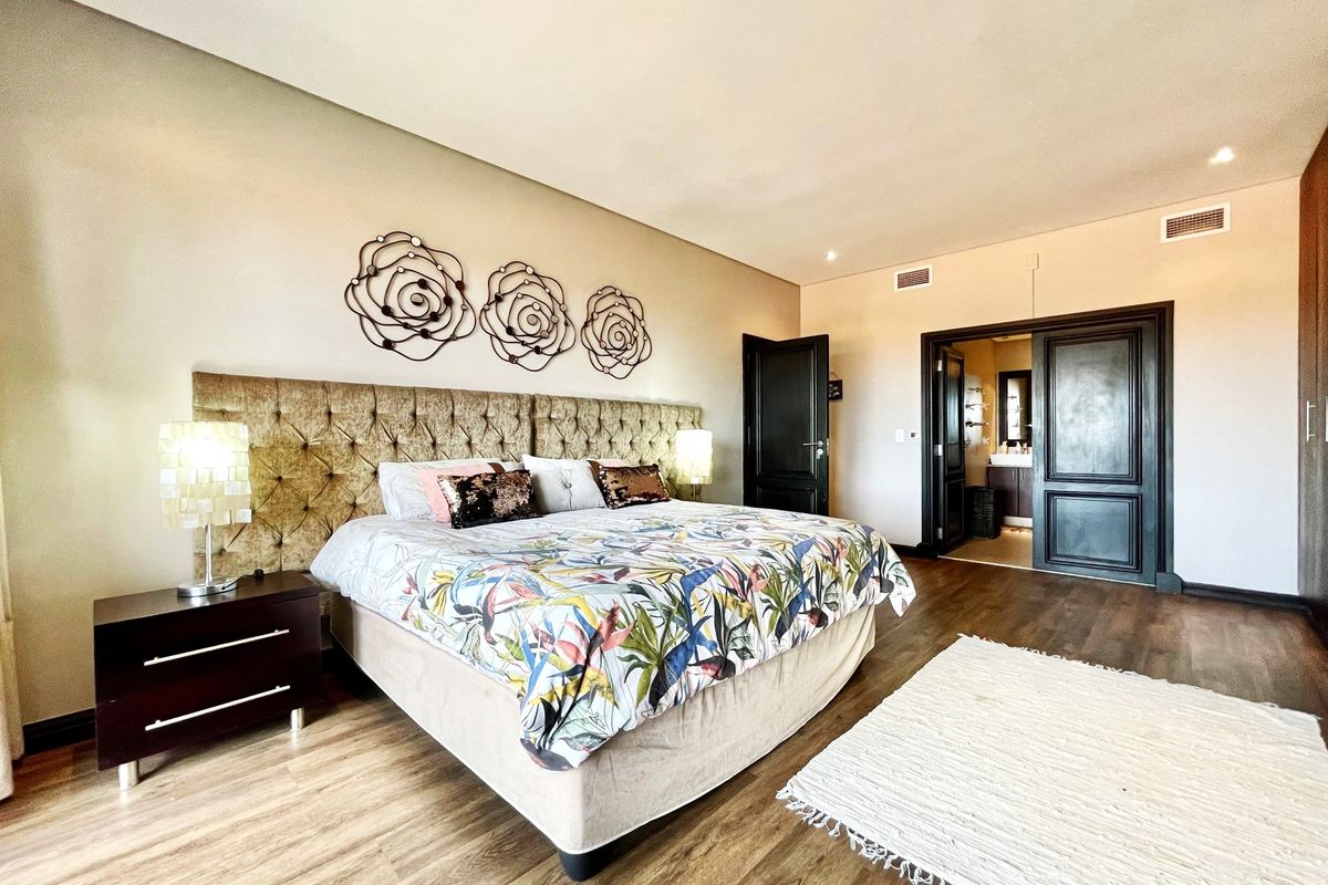 Spacious bedroom featuring wood-look flooring, recessed ceiling lighting, and an en-suite bathroom accessible through double doors.
