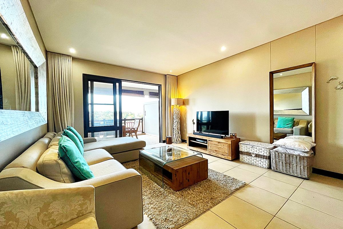 Spacious living room featuring large format floor tiles, recessed downlighting, and sliding glass doors providing seamless access to the outdoor balcony area.