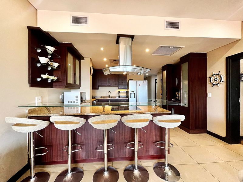 Modern open-plan kitchen featuring dark wood cabinetry, granite countertops, a breakfast bar, and a stainless steel extractor fan.
