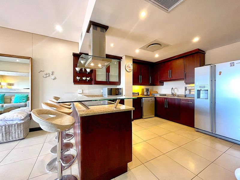 Modern open-plan kitchen featuring dark wood cabinetry, granite countertops, a breakfast bar, stainless steel extractor fan, and integrated lighting.