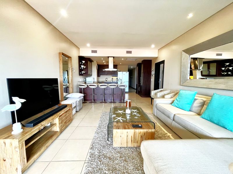 Open-plan living area featuring a modern kitchen with breakfast bar, tiled flooring, and recessed lighting, seamlessly flowing into the comfortable lounge space.