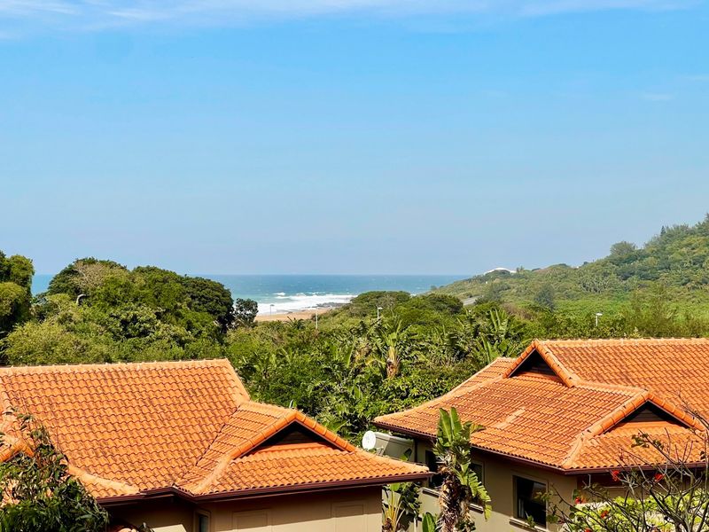 A scenic elevated view overlooking lush coastal vegetation and the ocean, featuring terracotta tiled roofs in the foreground.