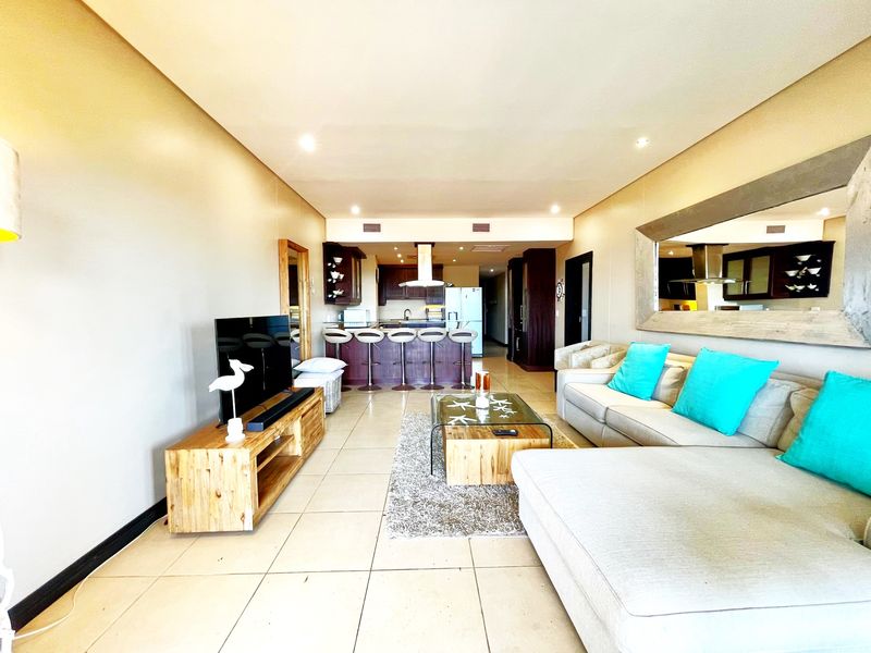 Open-plan living area featuring tiled flooring, recessed lighting, and a seamless transition to a functional kitchen with a breakfast bar.