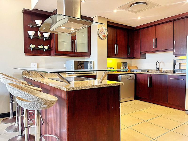 A well-appointed kitchen featuring dark wood cabinetry, granite countertops, a breakfast bar, and a modern stainless steel extractor fan.