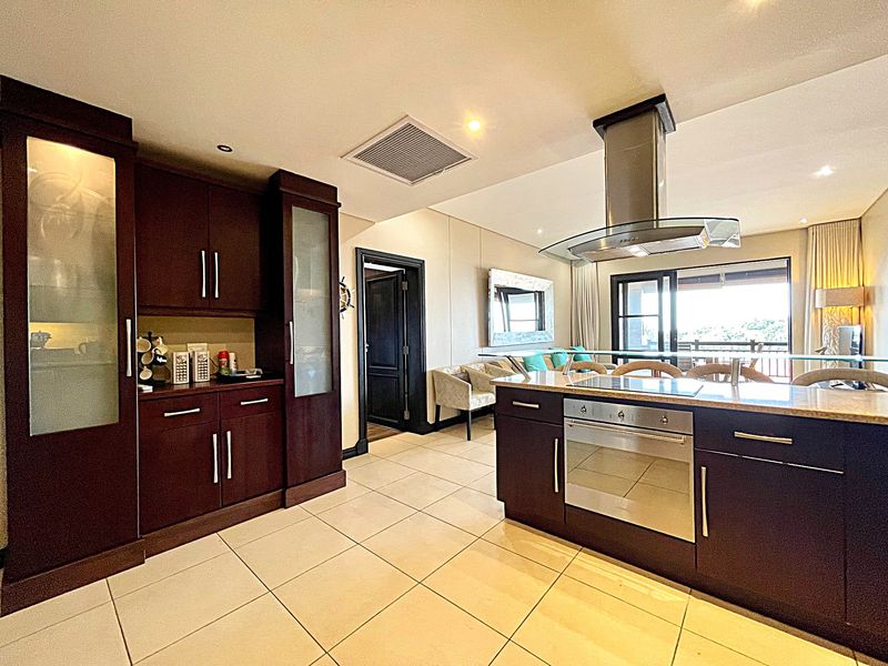 Open-plan kitchen featuring dark wood cabinetry, stone countertops, a built-in oven, and a stainless steel extractor fan, flowing into the living area.