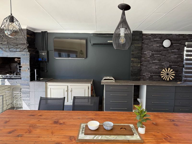 Covered patio area featuring a built-in braai, stone feature walls, modern cabinetry, and split-system air conditioning, ideal for outdoor entertaining.