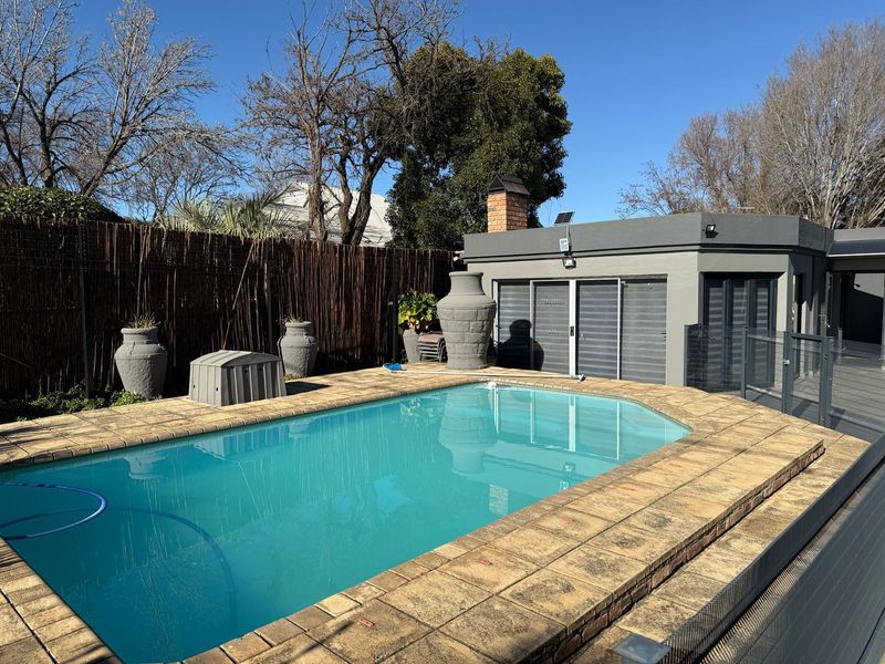 Outdoor pool area featuring a swimming pool with brick coping, adjacent to a structure with a brick chimney and sliding glass doors.