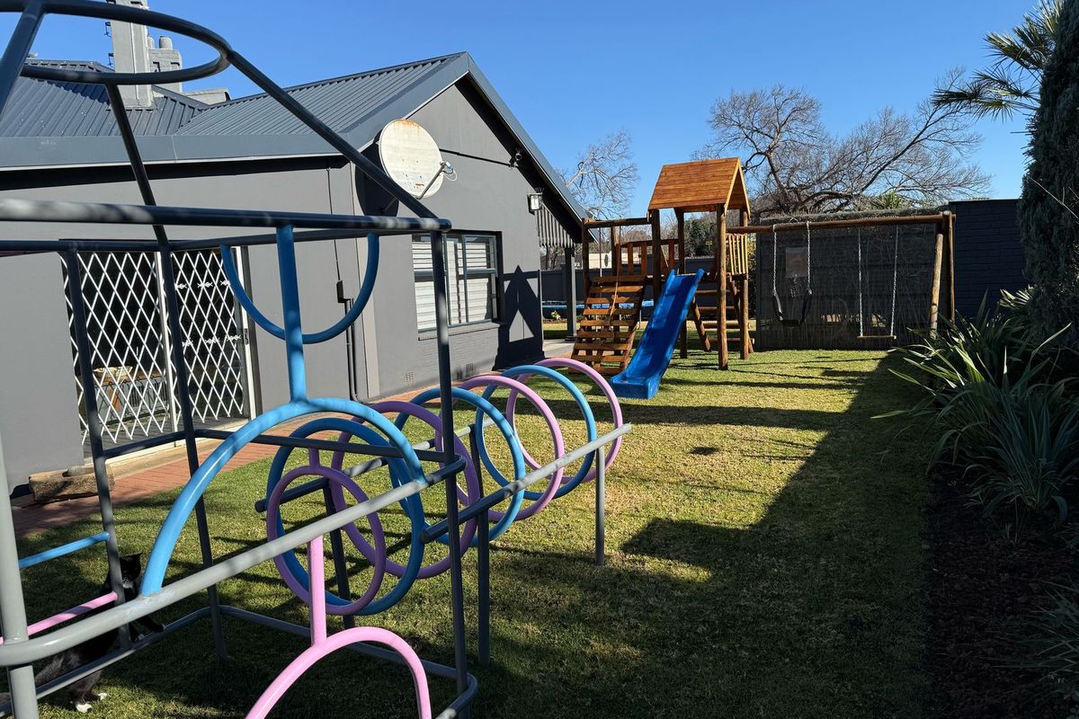 A view of the rear garden area featuring a well-maintained lawn, exterior wall with security gate, and metal roofing.