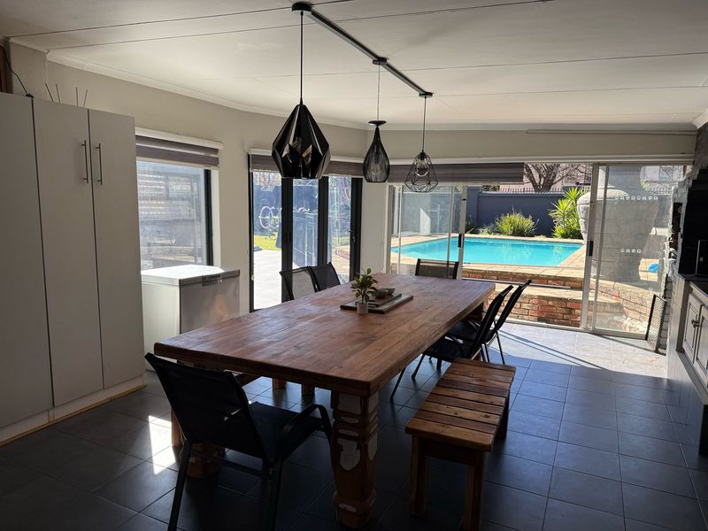 Spacious open-plan dining area featuring tiled floors, modern pendant lighting, and large sliding doors providing seamless access to the outdoor pool area.