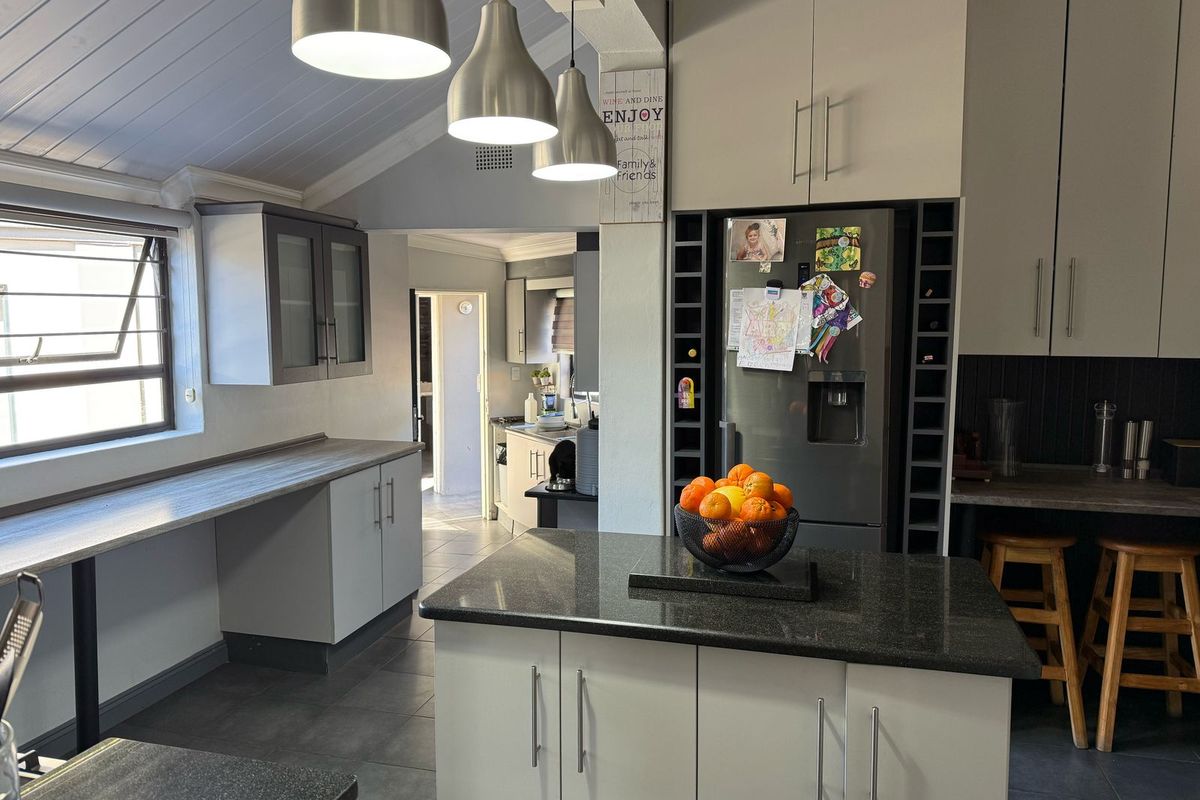Modern kitchen featuring granite countertops, ample cabinetry, a central island, and stylish pendant lighting under a vaulted ceiling.