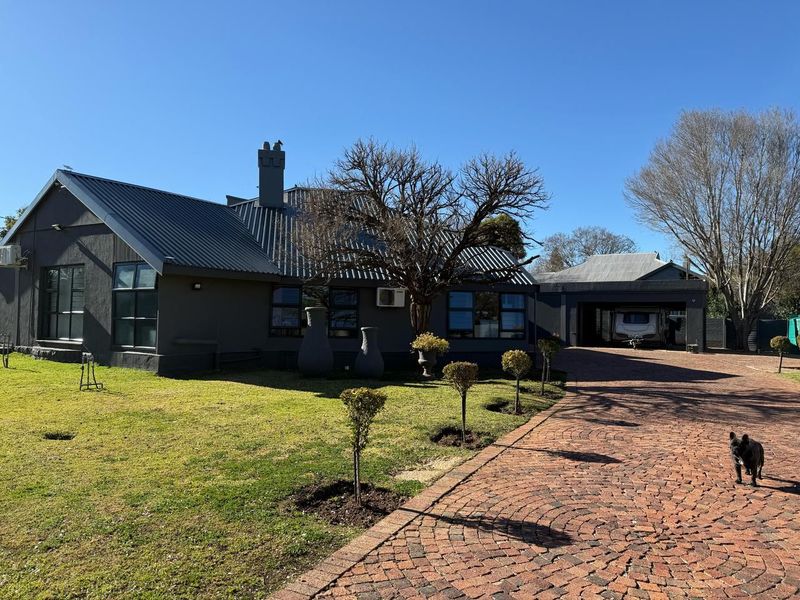 A well-maintained single-story home featuring a dark exterior finish, metal roofing, a paved brick driveway, and an attached carport.