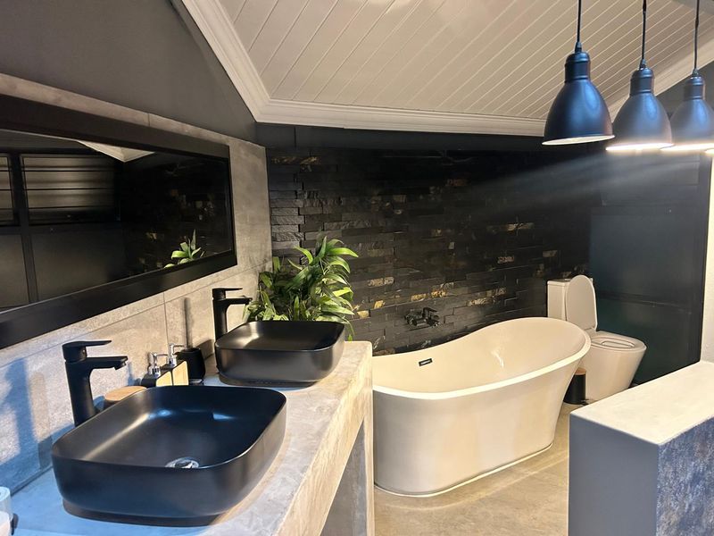 Modern bathroom featuring a double vanity with vessel sinks, a freestanding bathtub, and a striking stone feature wall under a vaulted ceiling.