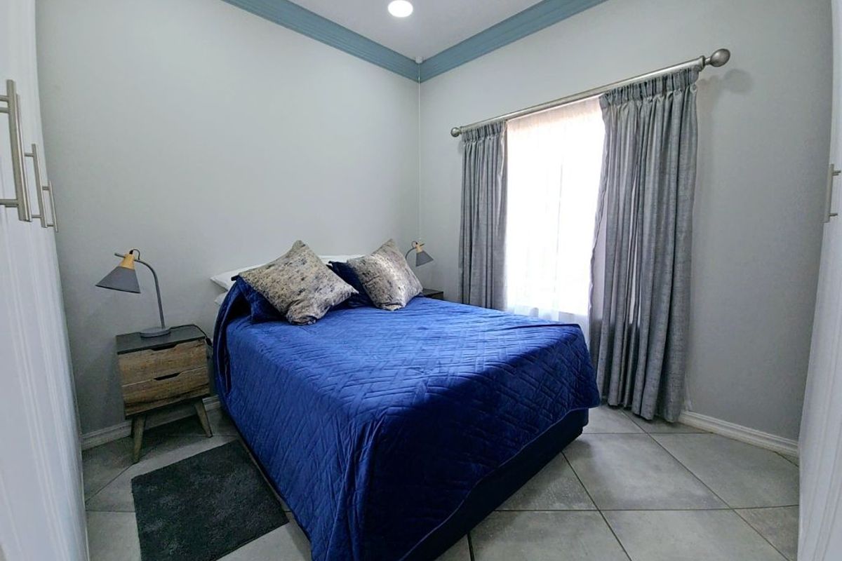 A well-maintained bedroom featuring tiled flooring, crown molding, and a large window with curtain rod.