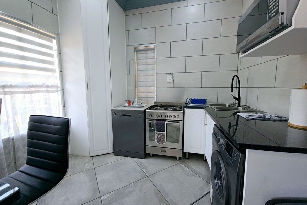 Modern kitchen featuring granite countertops, tiled walls, built-in cabinetry, a gas stove, and integrated laundry facilities.