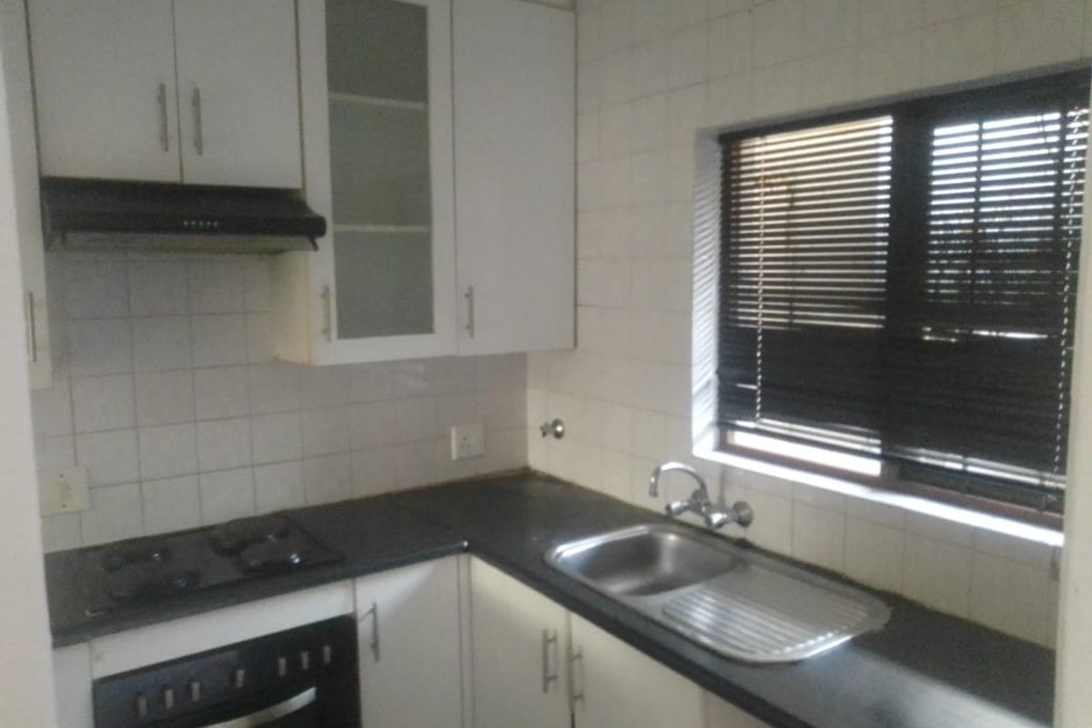 A functional kitchen featuring white cabinetry, dark laminate countertops, a built-in oven with gas hob, and a stainless steel sink with tiled backsplash.