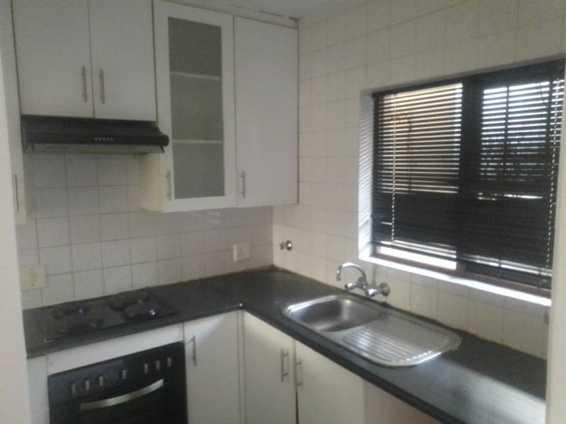A functional kitchen featuring white cabinetry, dark laminate countertops, a built-in oven with gas hob, and a stainless steel sink with tiled backsplash.