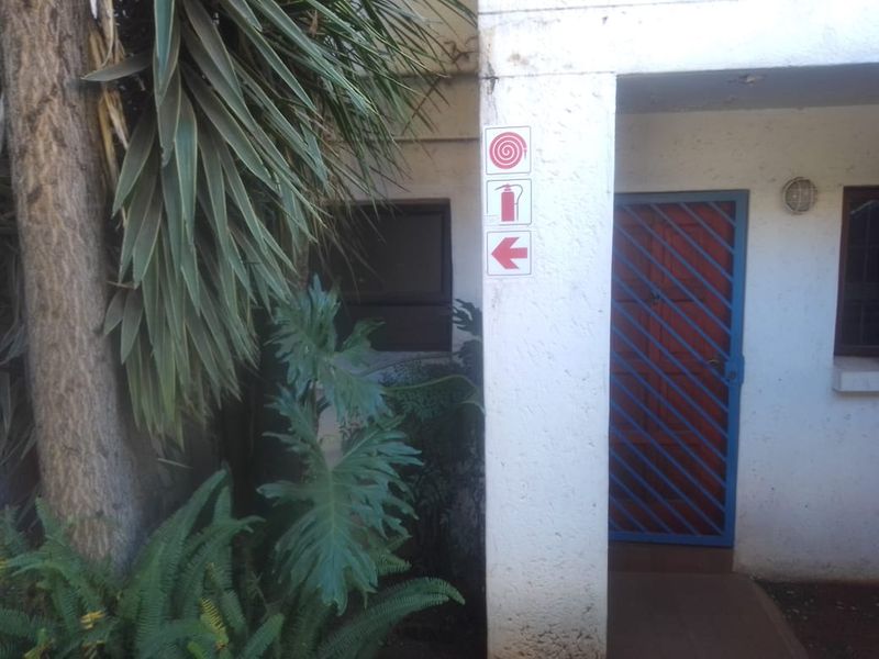 Entrance area of the townhouse featuring a blue security gate, exterior wall lighting, and fire safety signage.