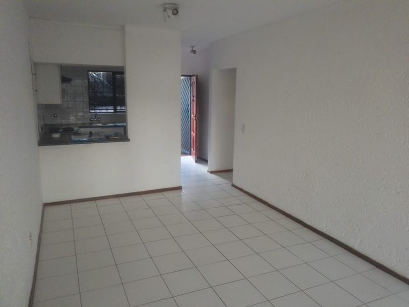 An empty open-plan living area featuring tiled flooring and a pass-through kitchen with built-in cabinetry and sink.