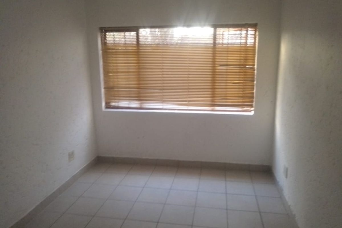 An empty bedroom featuring tiled flooring and fitted venetian blinds, offering a blank canvas for personalization.