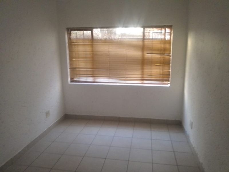 An empty bedroom featuring tiled flooring and fitted venetian blinds, offering a blank canvas for personalization.