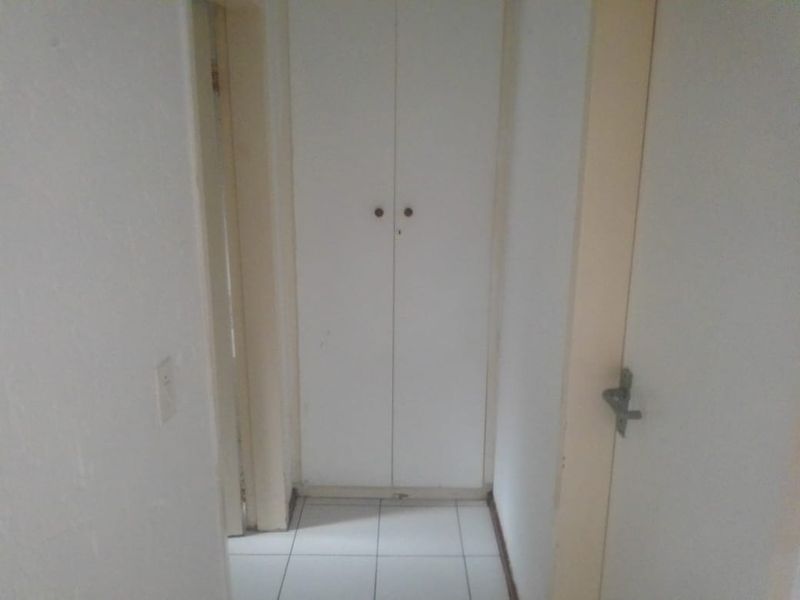 A narrow hallway featuring white tiled flooring and built-in storage cupboards, requiring minor cosmetic updates to improve the overall aesthetic.