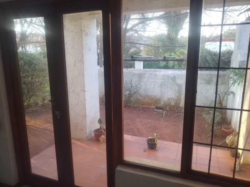 A covered patio area with tiled flooring and wooden door frames, overlooking a small private garden space with a masonry boundary wall.