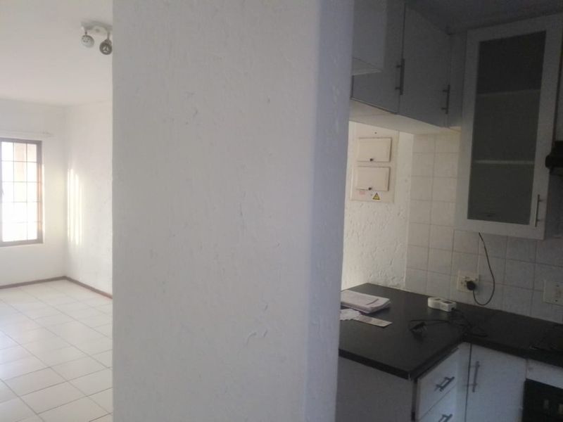 An open-plan living area featuring tiled floors and a compact kitchen with white cabinetry and dark countertops, currently vacant and ready for staging.