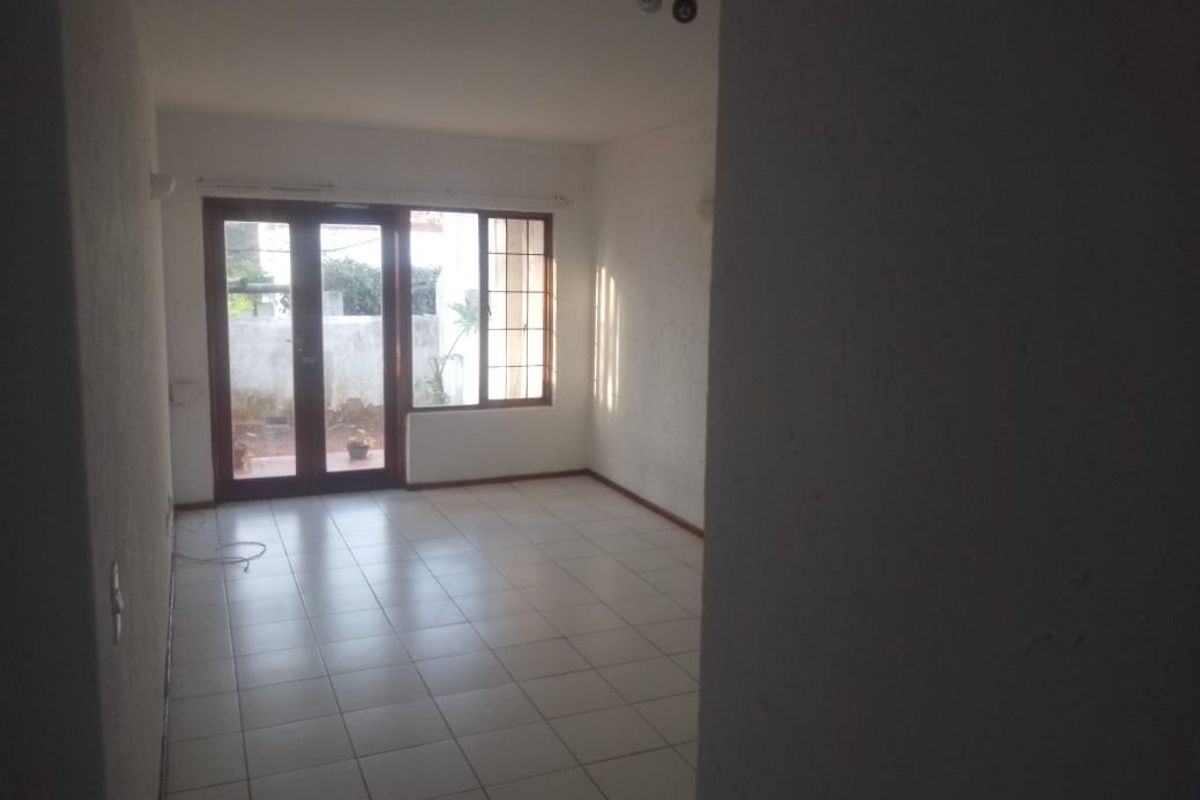 An empty living room featuring tiled flooring and large french doors that provide natural light and access to the exterior.