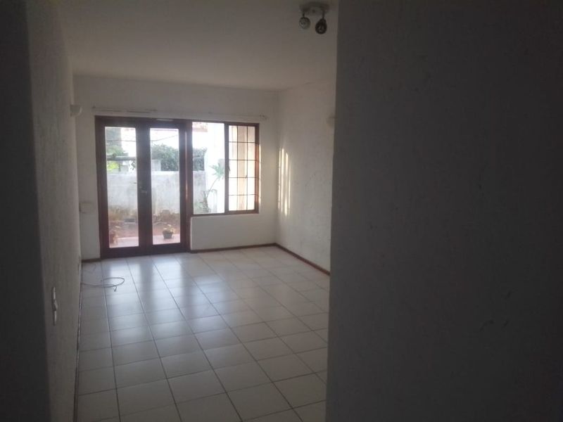 An empty living room featuring tiled flooring and large french doors that provide natural light and access to the exterior.