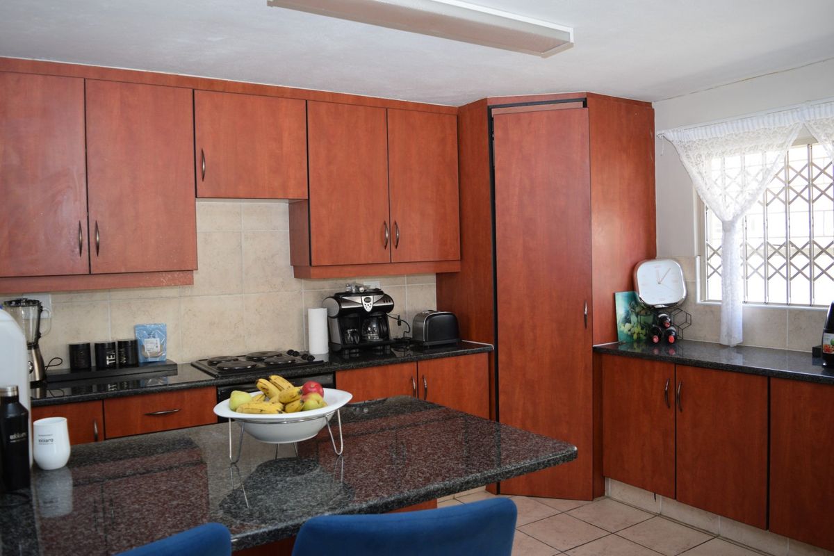 A functional kitchen featuring warm-toned built-in cabinetry, granite countertops, a gas hob, and a tiled backsplash with a security-fitted window.