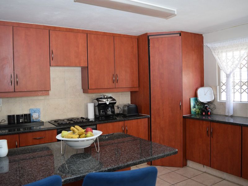 A functional kitchen featuring warm-toned built-in cabinetry, granite countertops, a gas hob, and a tiled backsplash with a security-fitted window.