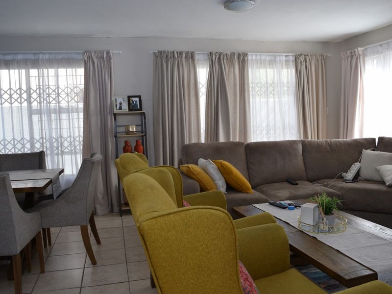 Open plan living and dining area featuring tiled flooring, large windows with security gates, and neutral wall finishes.