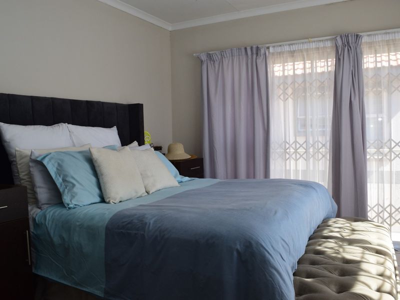 A well-lit bedroom featuring tiled flooring, neutral wall finishes, and a sliding glass door with an integrated security gate providing access to the exterior.