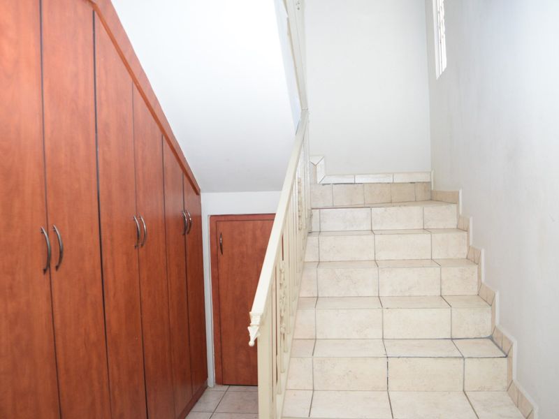 A functional hallway featuring a tiled staircase with a metal balustrade and integrated under-stair wooden storage cabinetry.