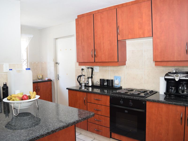 A functional kitchen featuring wood-finish cabinetry, granite countertops, a built-in oven, and an electric hob with a tiled backsplash.
