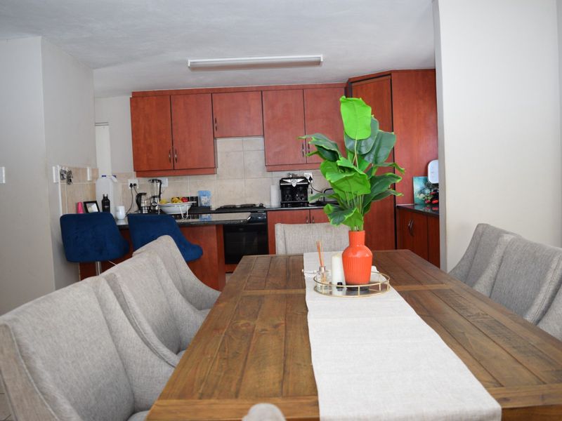 Open plan kitchen and dining area featuring wooden cabinetry, built-in oven and hob, and tiled backsplash.
