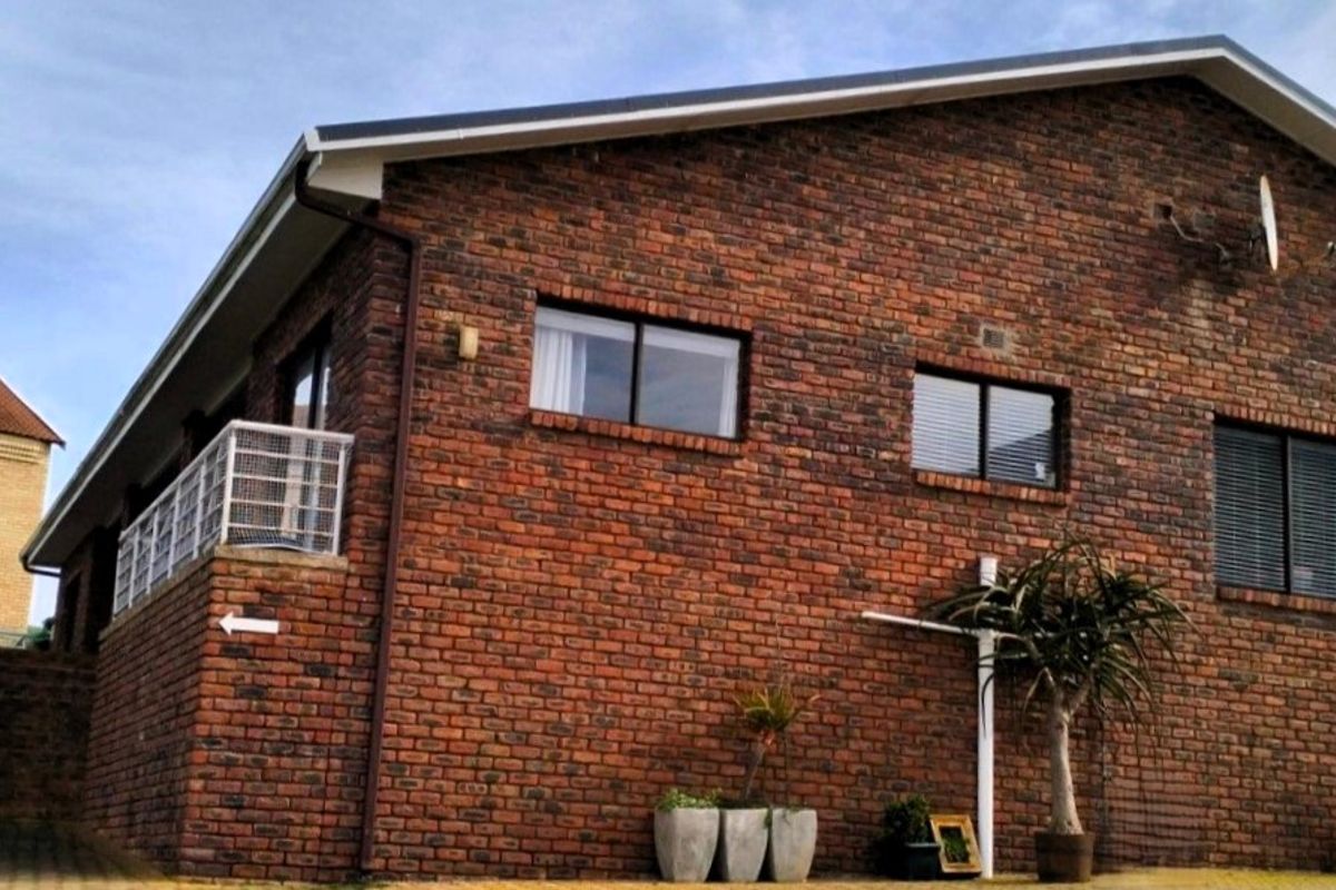 A side view of a face brick house featuring aluminium window frames, guttering, and a satellite dish mounted on the exterior wall.