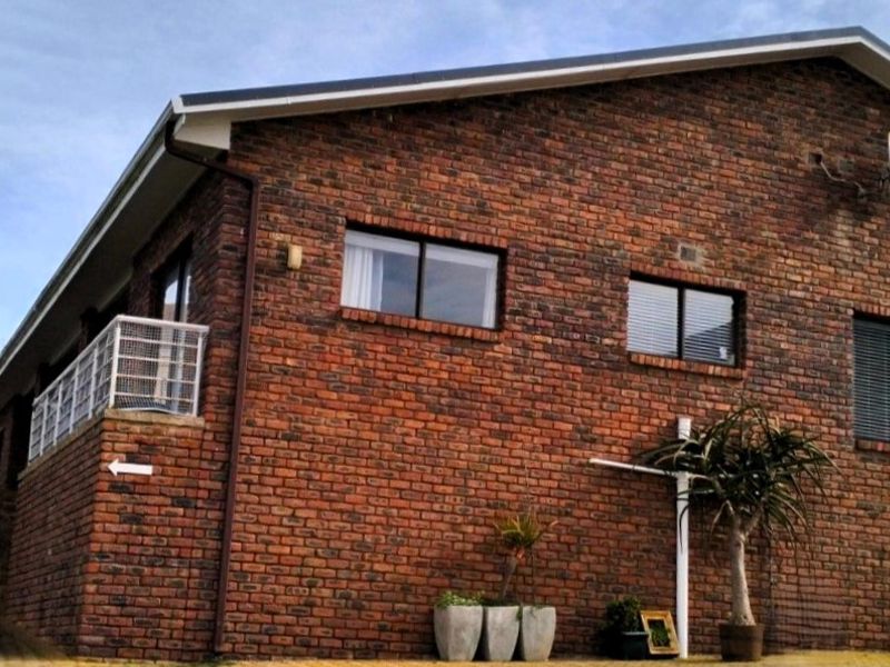 A side view of a face brick house featuring aluminium window frames, guttering, and a satellite dish mounted on the exterior wall.