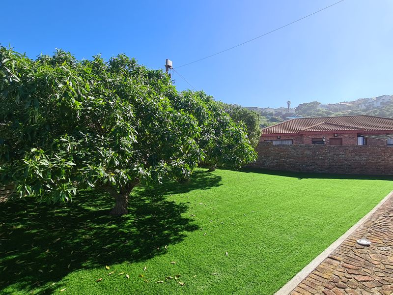 A well-maintained garden area featuring artificial turf, a paved walkway, and a brick boundary wall.