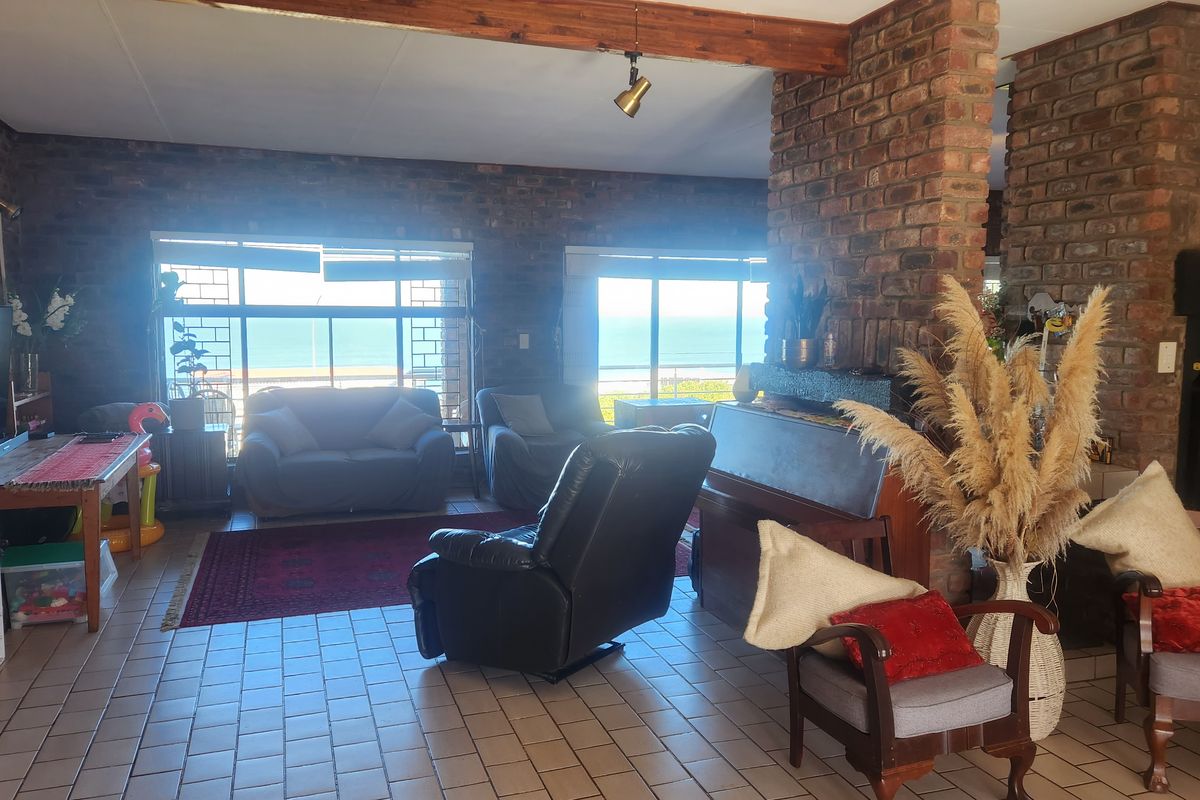 Spacious living room featuring exposed brick walls, a timber ceiling beam, tiled flooring, and a built-in fireplace with expansive ocean views.